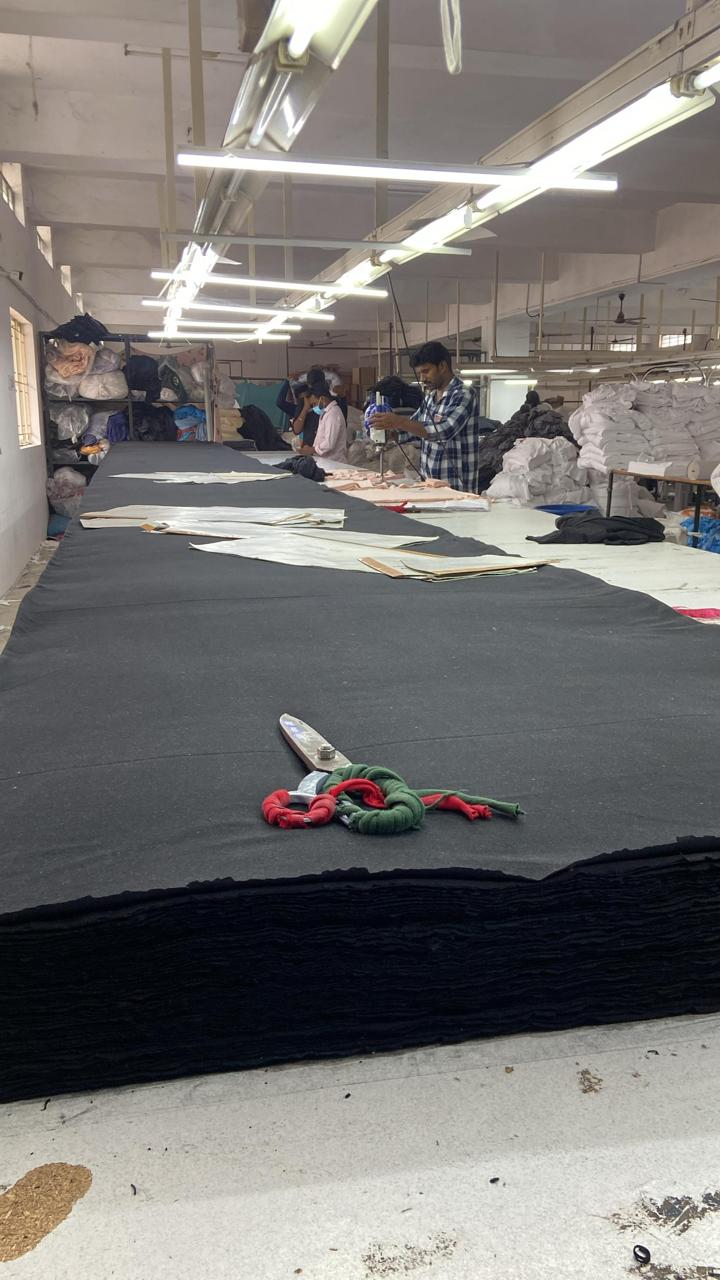 Interior of an apparel manufacturing facility with workers handling fabric and patterns on a cutting table.